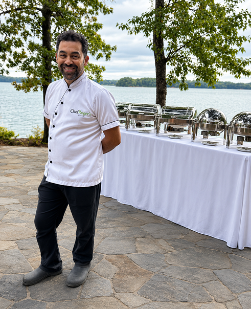 Chef Roger standing beside an outdoor buffet overlooking a lake